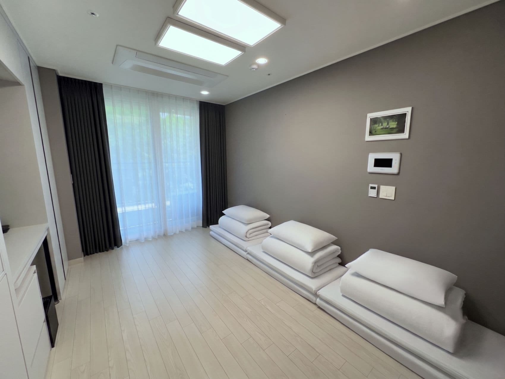 Habitación de hotel con una ventana grande, televisión de pantalla plana, termostato y toallas ordenadas.