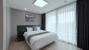 Ein modernes Hotelzimmer mit einem großen Bett, einem Kopfteil, einem Bild an der Wand und Blick durch transparente Vorhänge.
