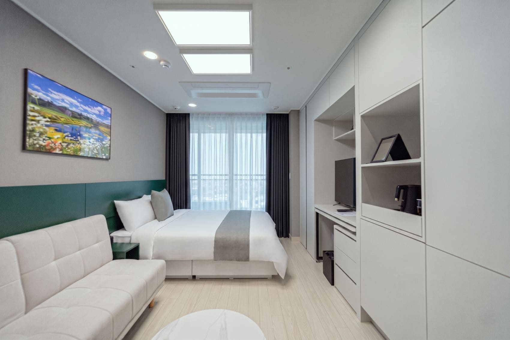 A modern hotel room with a bed, a sofa, a desk, and a TV.