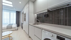 Eine moderne Küche mit integriertem Waschmaschine, einem Essbereich mit rundem Tisch und einem großen Fenster mit Vorhängen.