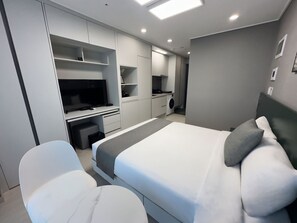 A modern bedroom with a bed, a TV, a desk, and a washing machine. - Bella Stay Hotel (Chuncheon)