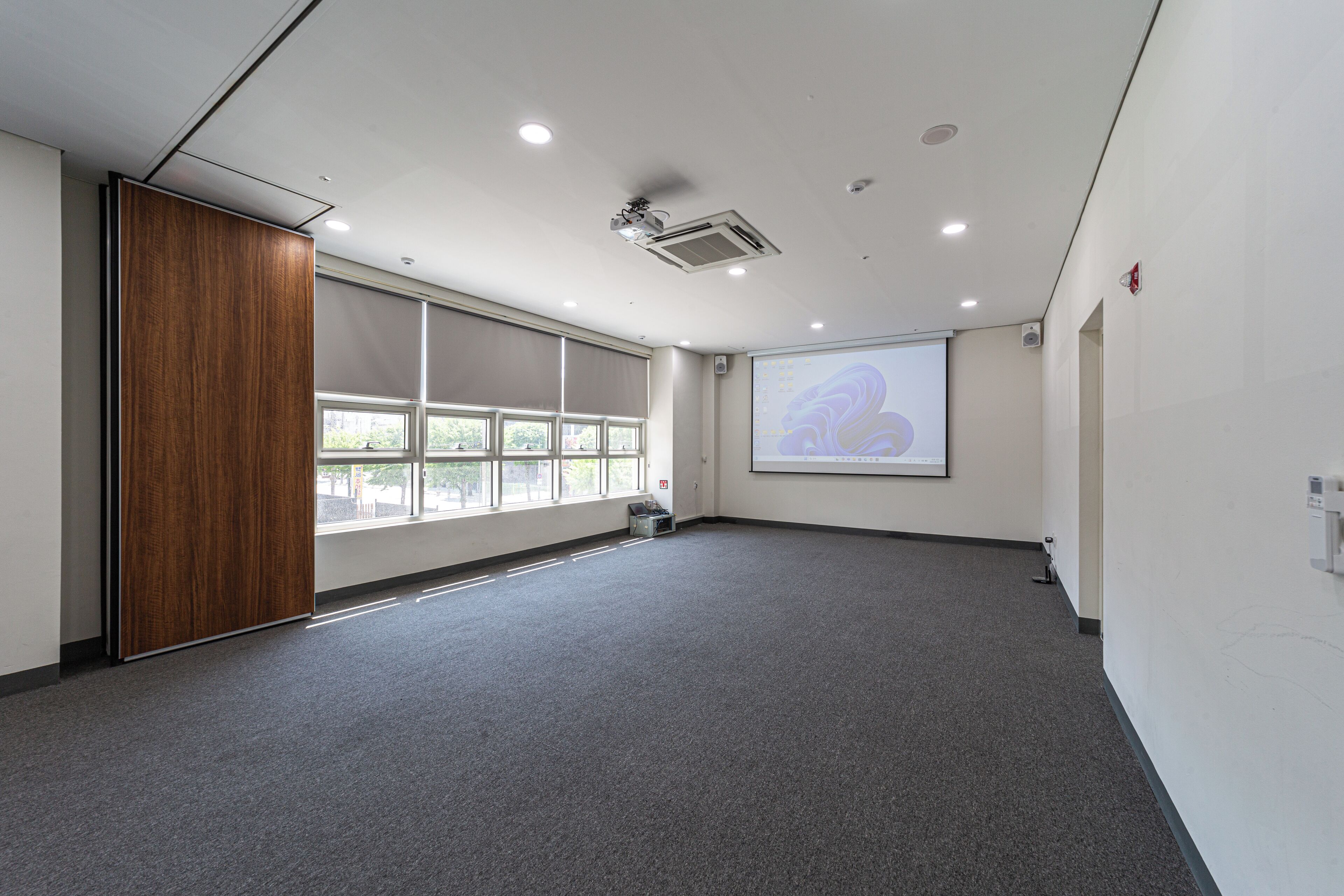 A conference room with a large projection screen, a wooden panel, and a carpeted floor.