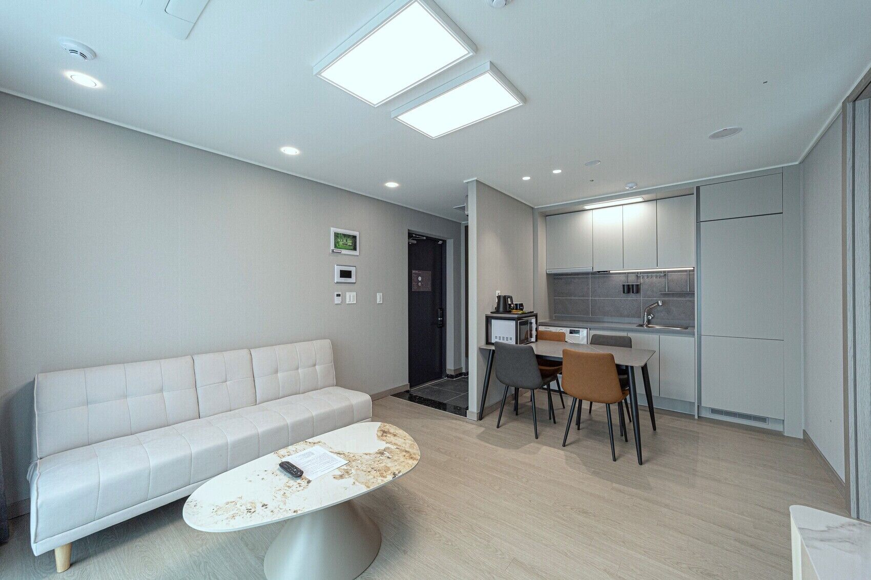 Una sala de estar moderna con sofá, una mesa de comedor con sillas, una zona de cocina con armarios e iluminación empotrada en el techo.