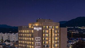 Ein mehrgeschossiges Hotel mit einem gut sichtbaren 'Bella Stay' Schild, das modernes Architektur mit flachem Dach und zahlreichen Fenstern aufweist.