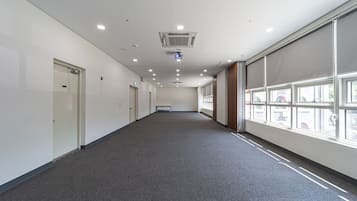 A long, narrow hallway with white walls, grey carpet, and large windows on one side.