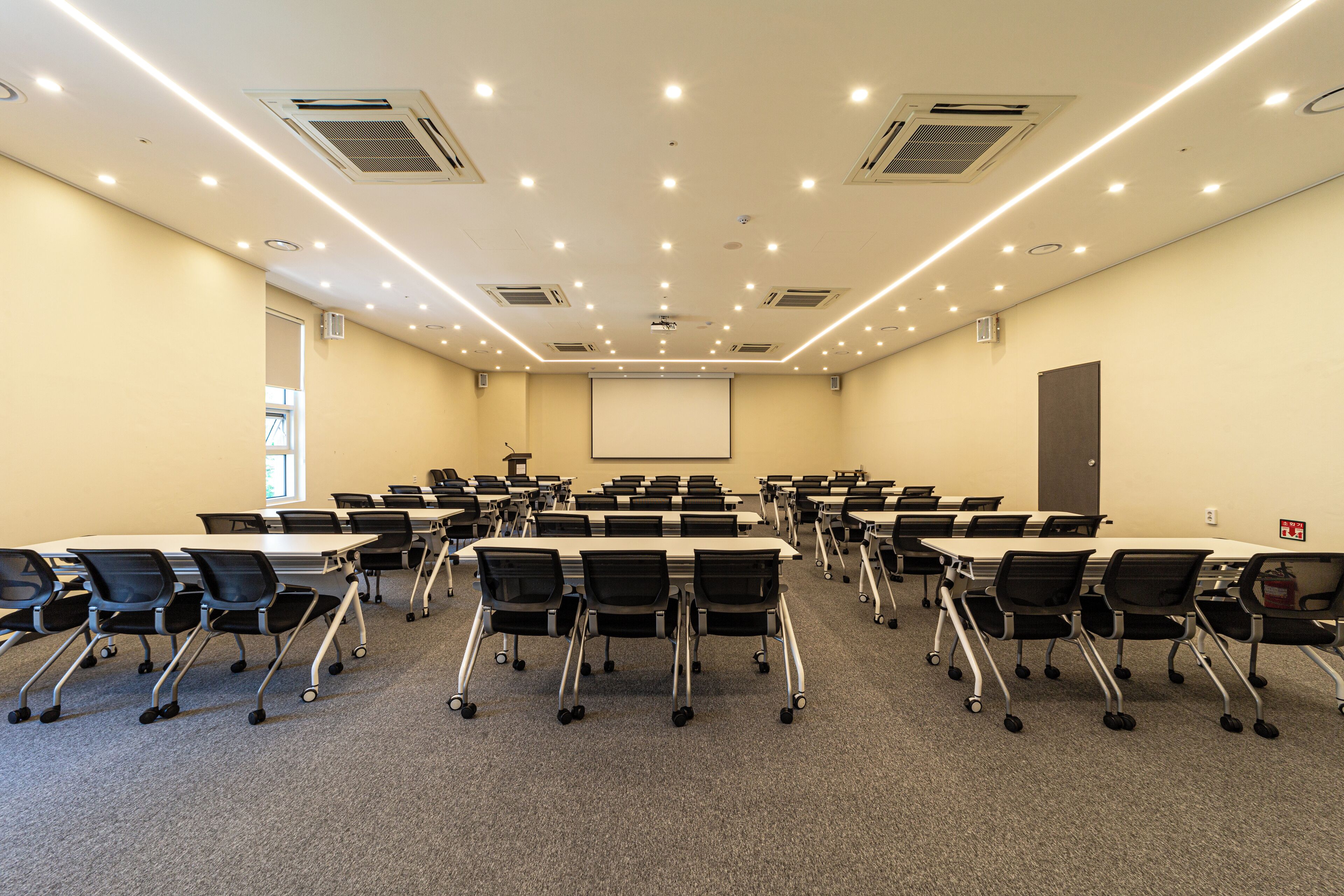 A conference room with multiple tables and chairs, equipped with projectors and air conditioning vents.