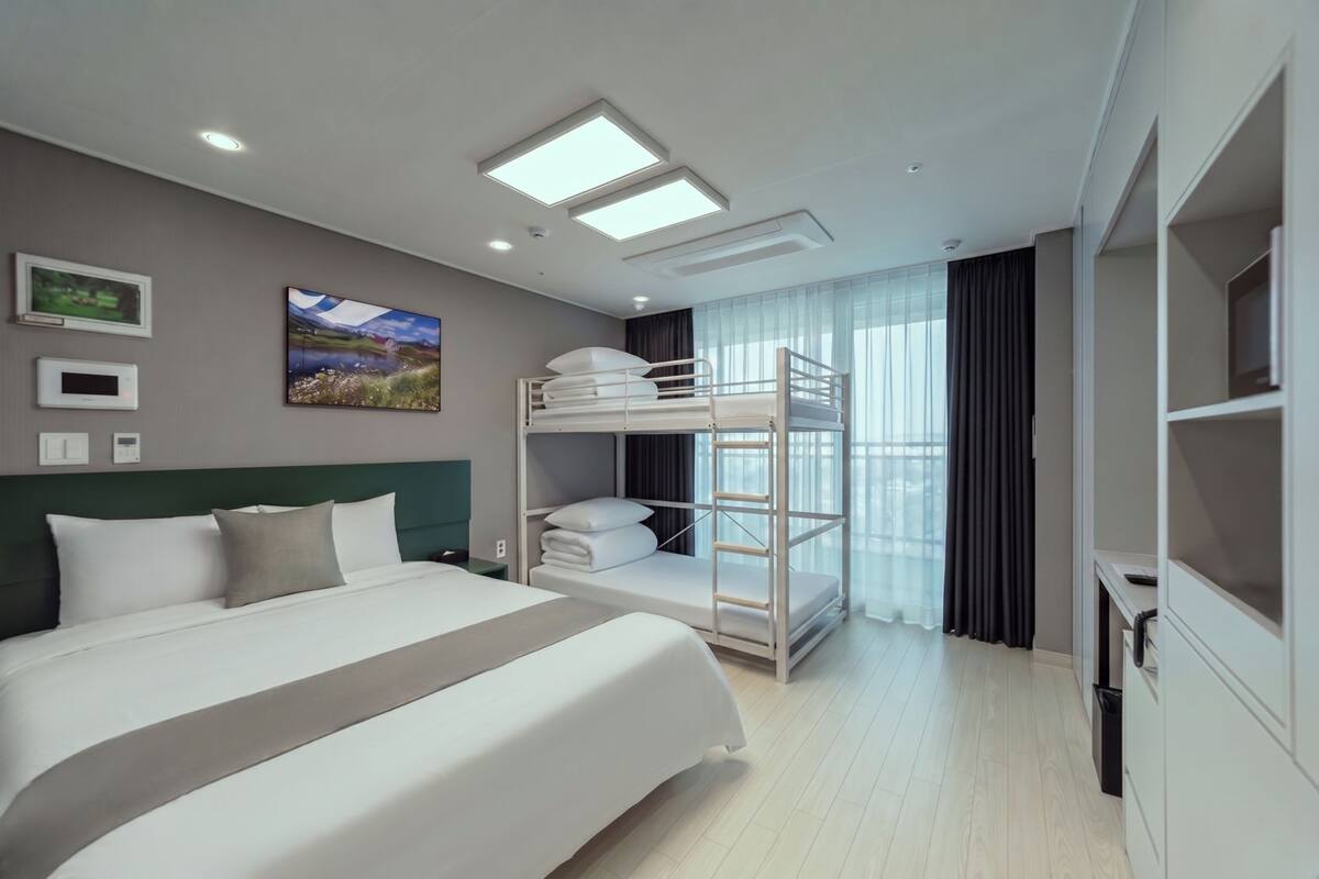 A modern hotel room with a large bed, bunk beds, a flat-screen TV, and a view of the city.