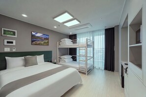 A modern hotel room with a large bed, bunk beds, a flat-screen TV, and a view of the city. - Bella Stay Hotel (Chuncheon)