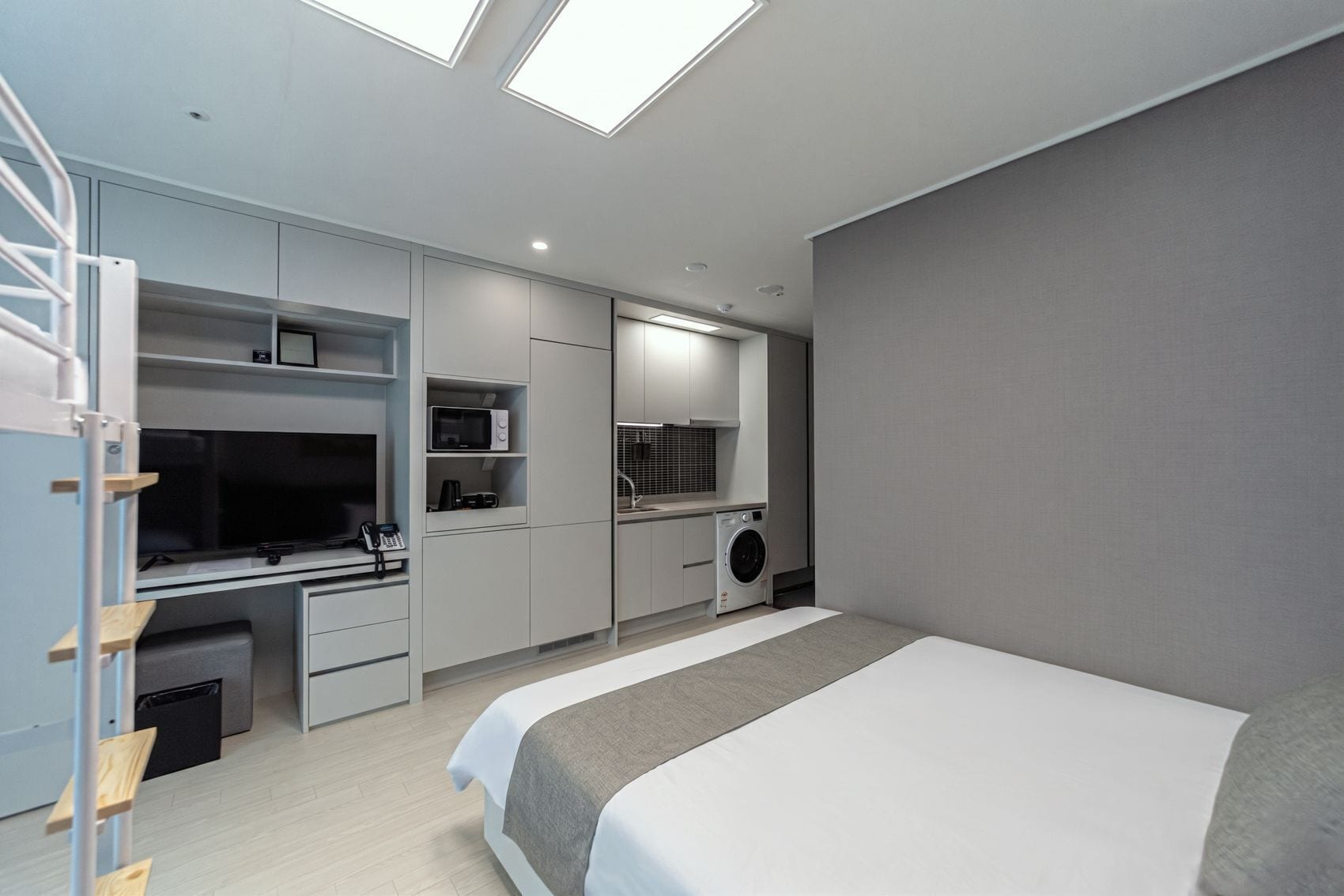 Ein modernes Schlafzimmer mit Bett, Schreibtisch mit Computer, Waschmaschine und einem Oberlicht.