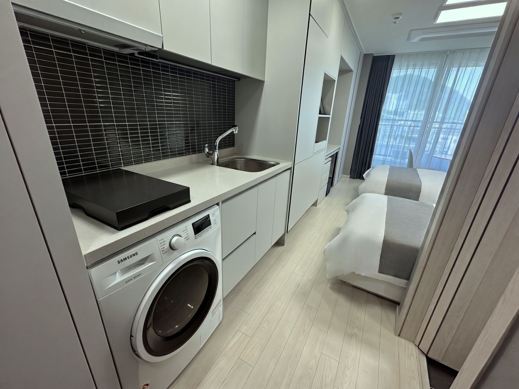 A modern kitchen with a washing machine, a sink, and a black tiled backsplash.