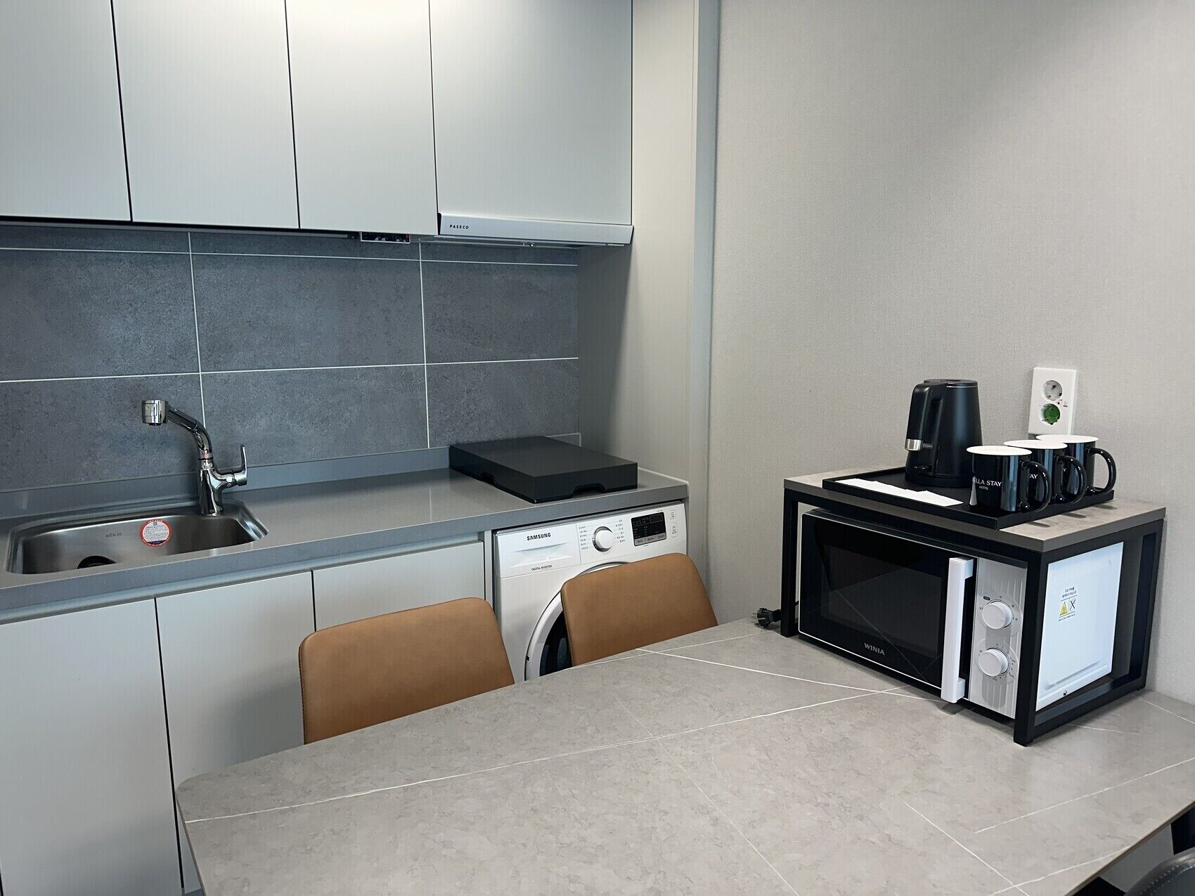 Una kitchenette compacta equipada con microondas, cafetera y un lavamanos pequeño.