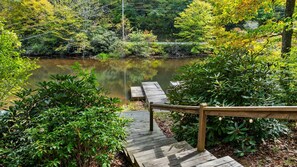 A wooden deck leading to a calm pond surrounded by lush greenery.