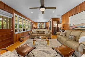 A spacious living room with a large window, a ceiling fan, and a beige sofa.