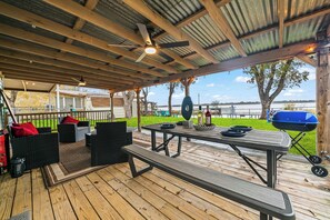 Une terrasse extérieure dotée d’un espace salon couvert, d’un barbecue et offrant une vue sur un plan d’eau.