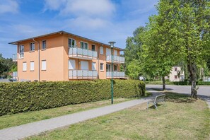 Ein mehrstöckiges Wohngebäude mit Balkonen, einem gepflasterten Weg und einer Hecke.