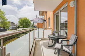 A balcony with a glass railing, a table with chairs, a striped umbrella, and a potted plant.