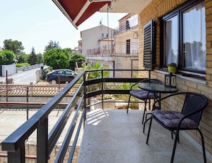 A balcony with two chairs and a table, a car parked outside, and a building with a brick facade in the background. - Apartments Pjescana Uvala/istrien 11044 (Medulin)