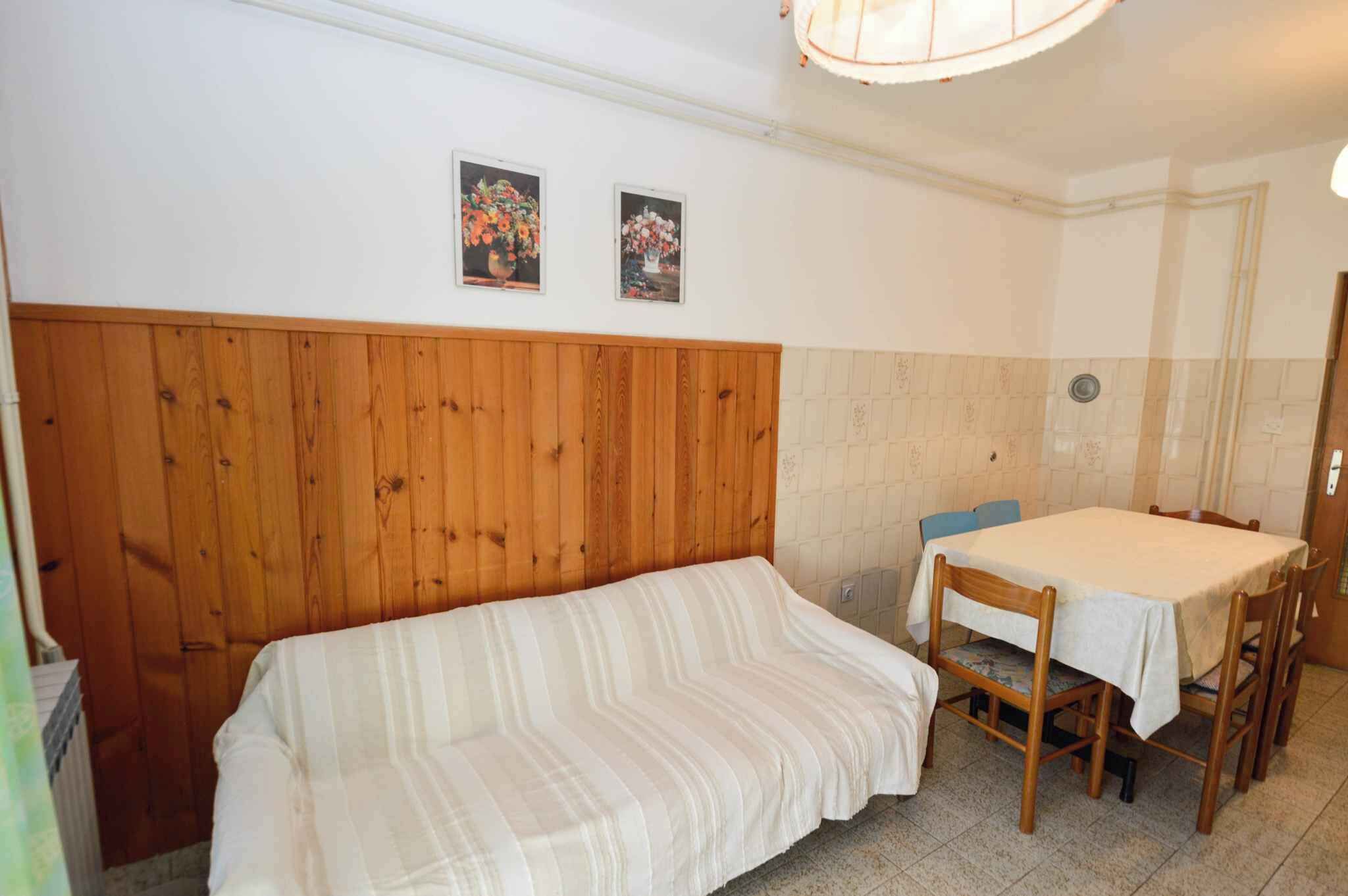 A room with a wooden headboard, a striped sofa, a dining table with chairs, and two framed pictures on the wall.