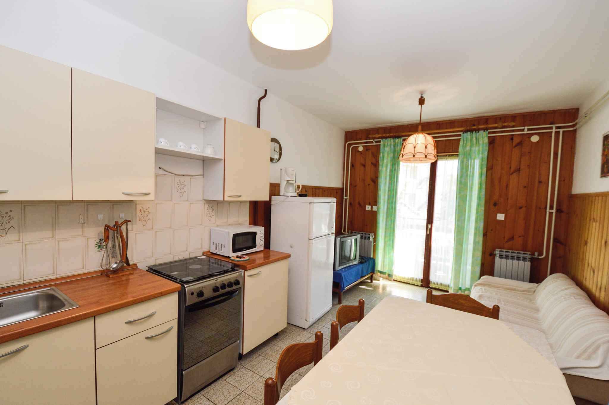 Cocina compacta con estufa, microondas, refrigerador y pileta. Hay una mesa de comedor con sillas y una cama en la habitación contigua.