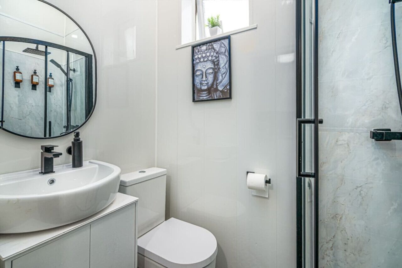 A modern bathroom with a round mirror, white sink, toilet, and shower.