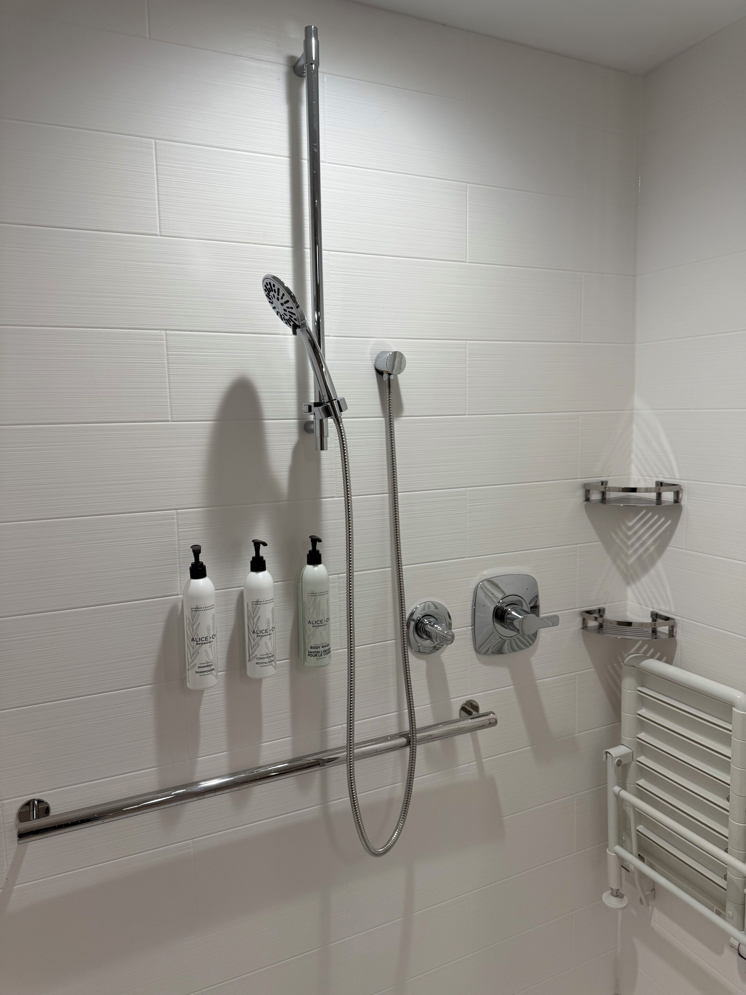 A modern bathroom with a shower, two shampoo bottles, a towel rack, and a radiator.