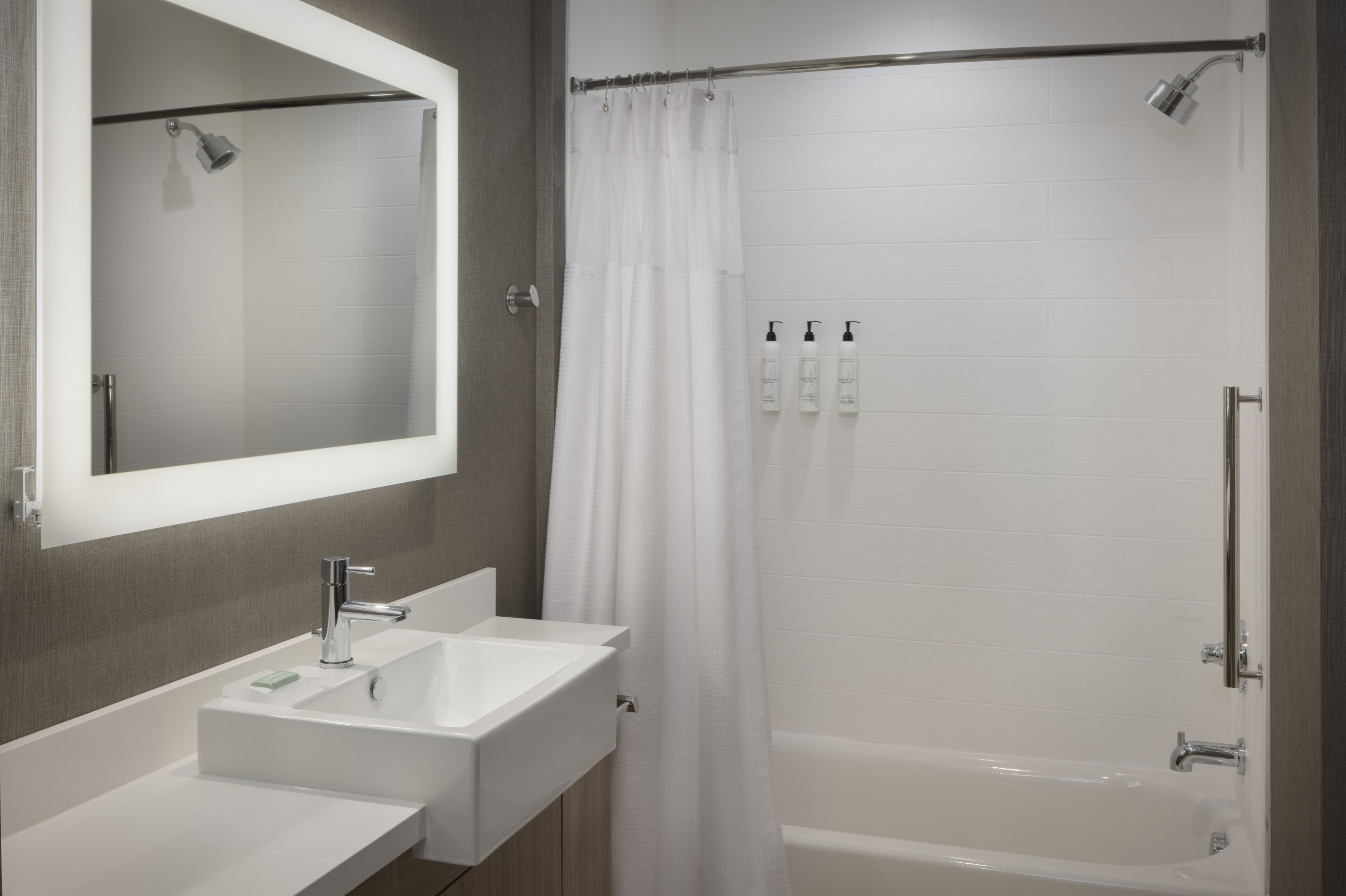Une salle de bain moderne avec un double vasque, un grand miroir, une douche avec rideau et une baignoire.