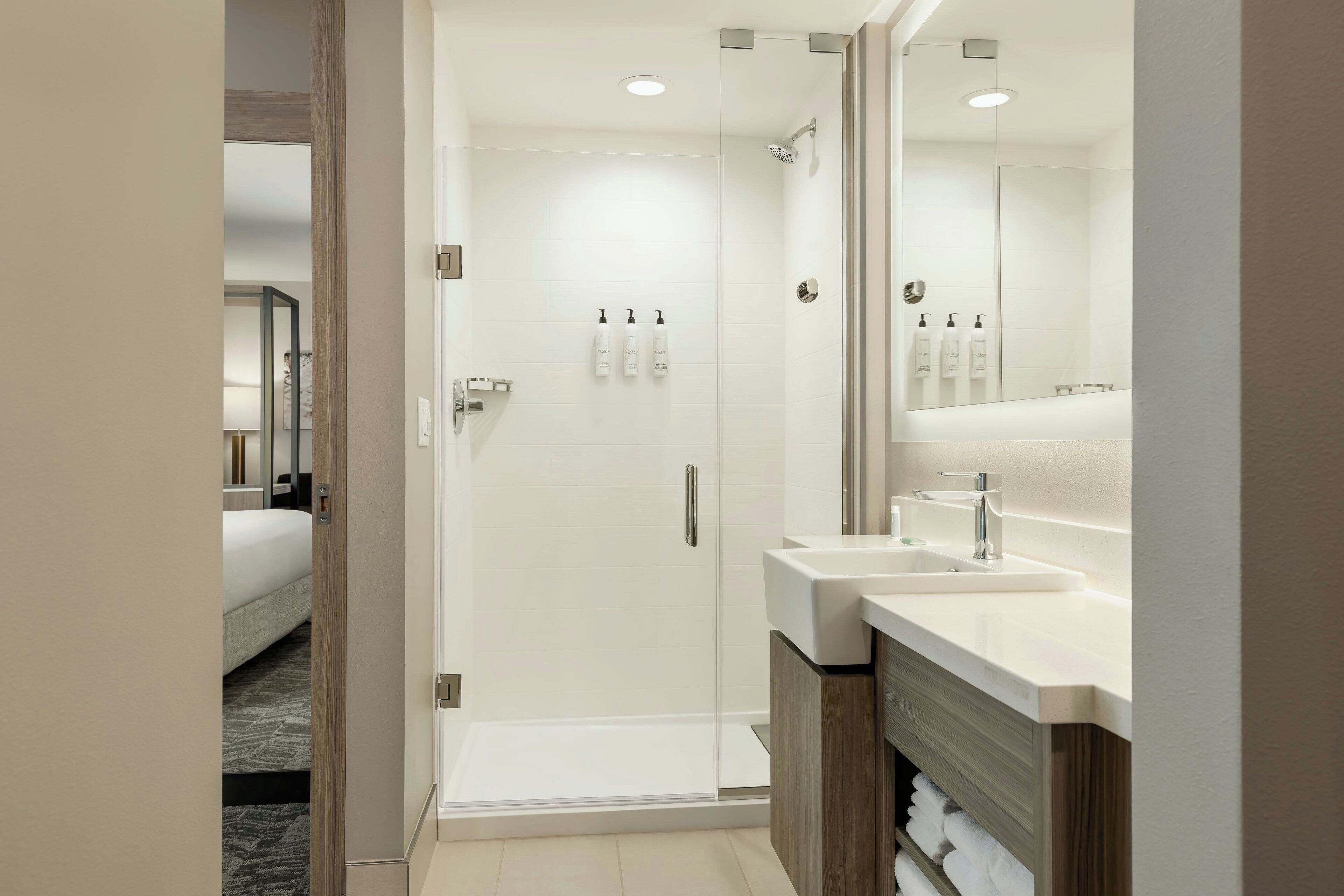 A modern bathroom with a glass shower enclosure, a large mirror, and a vanity with a sink.