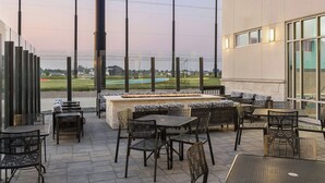 Un espace extérieur aménagé en terrasse, avec des sièges et des tables, offrant une vue sur un jardin paysager et un terrain de golf.