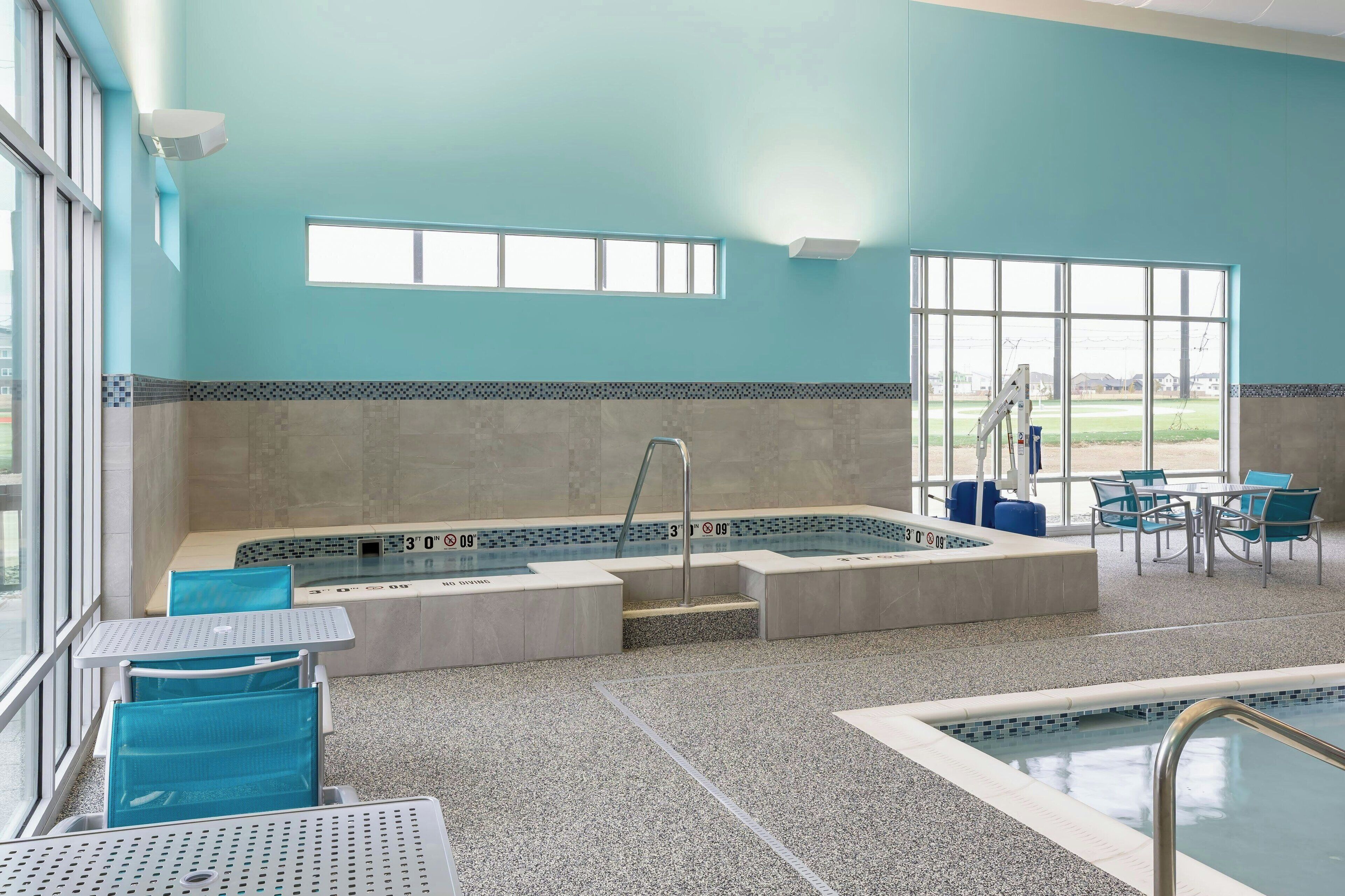 A swimming pool area with a jacuzzi, seating, and a view of the outdoors.