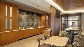 Un hall d’hôtel moderne avec un comptoir d’accueil en bois, un mur en briques et un espace détente comprenant des tables et des chaises.