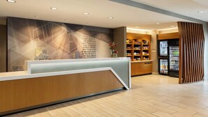 Un espace d’accueil moderne, doté d’un comptoir de réception en bois, d’un mur orné de motifs géométriques et d’un réfrigérateur rempli de boissons.