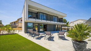 Une maison moderne à deux étages, dotée d’un balcon, d’une piscine et d’un espace salon extérieur.