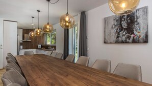 Een moderne eetruimte met een houten tafel, meerdere stoelen, hanglampen en een groot abstract schilderij aan de muur.