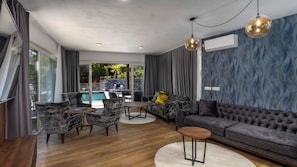 Un salon moderne avec vue sur la piscine, doté d’un canapé gris, de fauteuils en marbre et d’une table basse ronde.
