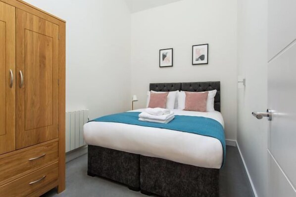 Een slaapkamer met een bed, een kledingkast en twee foto's in lijsten aan de muur.