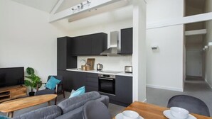 Una sala de estar moderna con un sofá, una mesa de centro y un televisor. Hay una zona de cocina con armarios y electrodomésticos.