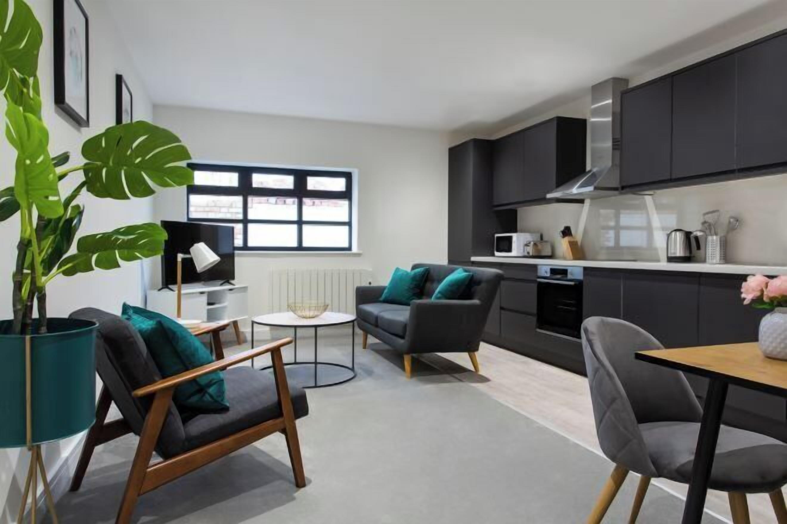 A modern living room with a sofa, a coffee table, and a dining table. There is a large potted plant and a window with blinds.