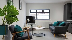 Una sala de estar moderna con sofá, sillón y una planta grande en maceta.