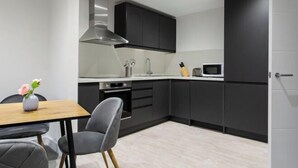 Una cocina moderna con armarios oscuros, una campana extractora de acero inoxidable, un microondas y un comedor con mesa y sillas.