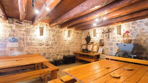 Une pièce rustique aux murs de pierre, avec des bancs et des tables en bois, une cheminée en pierre et un plafond en bois.