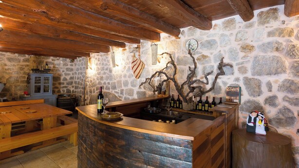 Une cuisine rustique aux murs de pierre, avec un bar en bois, un plan de travail en pierre et un plafond en bois rustique.