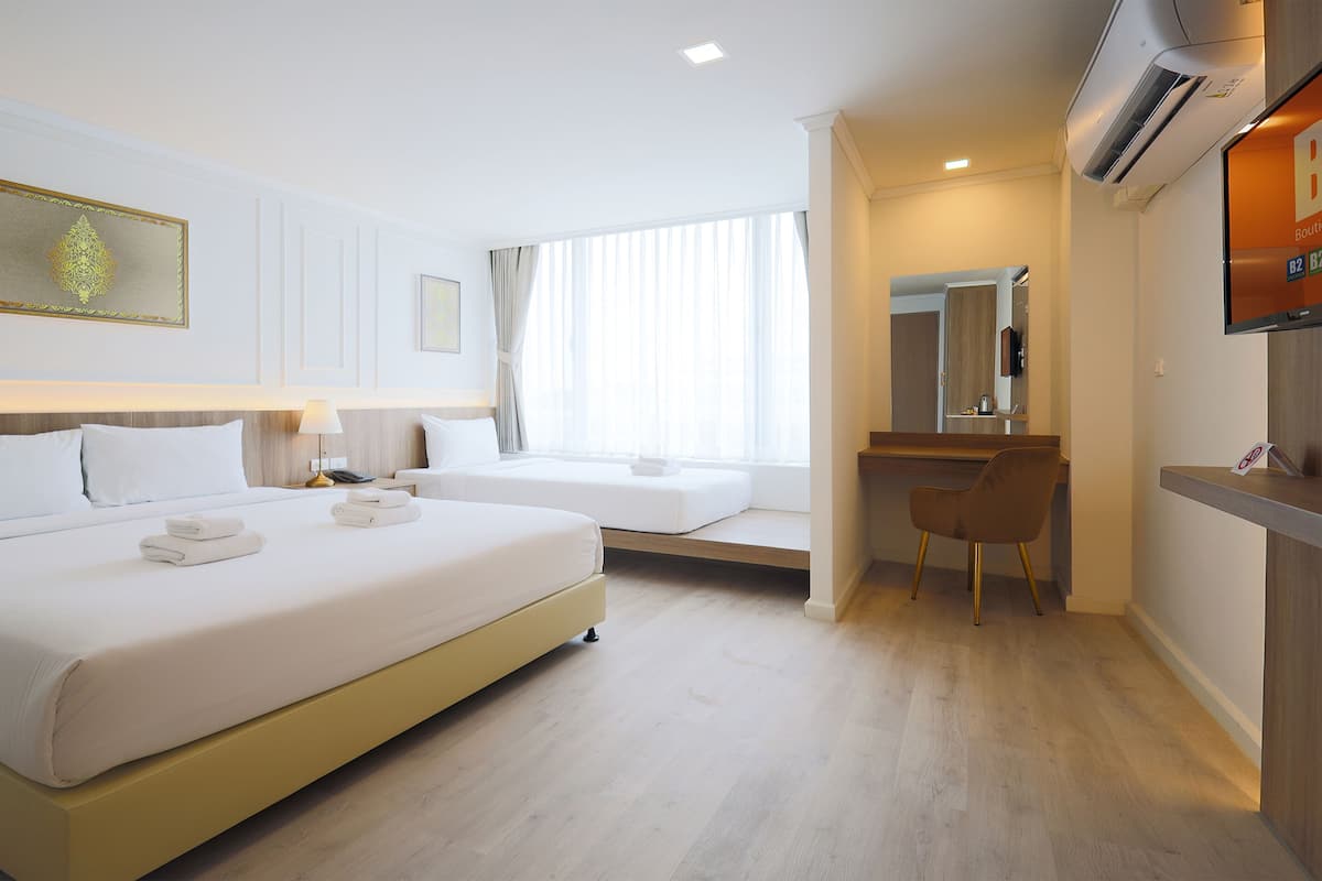 Quarto de hotel com cama, mesa de cabeceira, luminária e escrivaninha com cadeira.