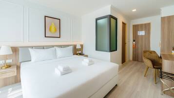 A hotel room with a large bed, bedside tables with lamps, a desk with a chair, a framed picture on the wall, and a door with a sign.