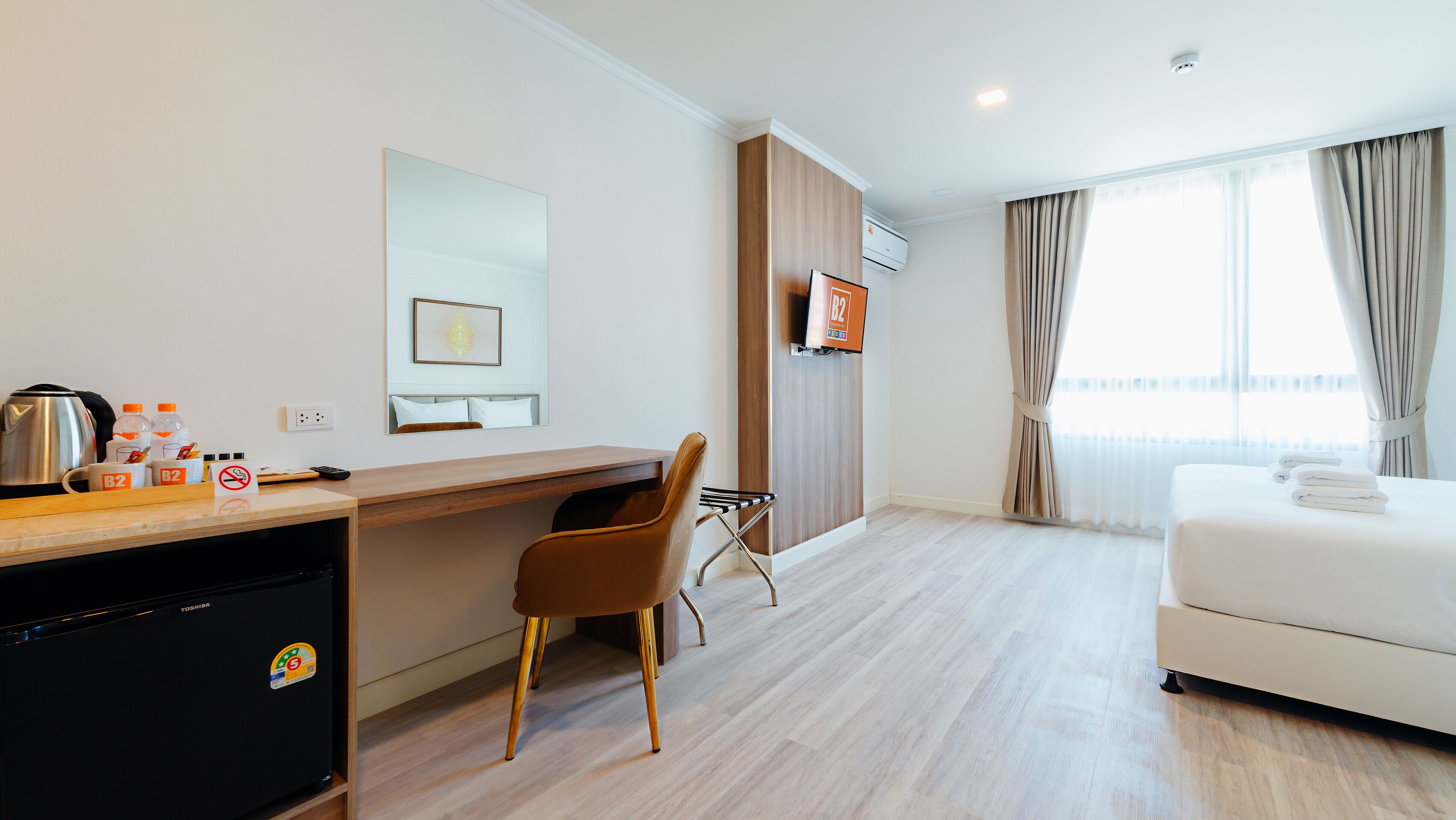 Ein Hotelzimmer mit Holztisch, Stuhl, Bett, Fernseher und einem Fenster mit Vorhängen.