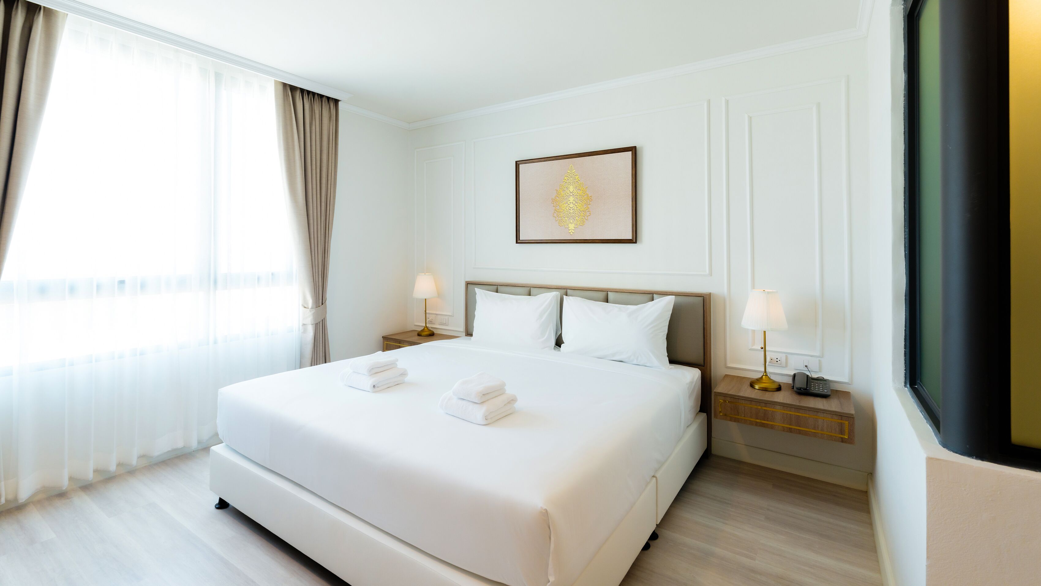 A hotel room with a large bed, two bedside tables, a framed picture on the wall, and a window with curtains.