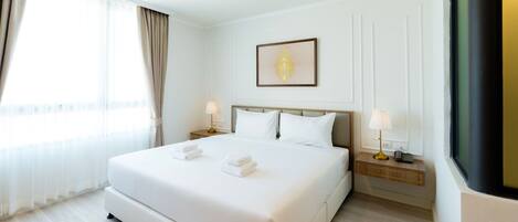 A hotel room with a large bed, two bedside tables, a framed picture on the wall, and a window with curtains.