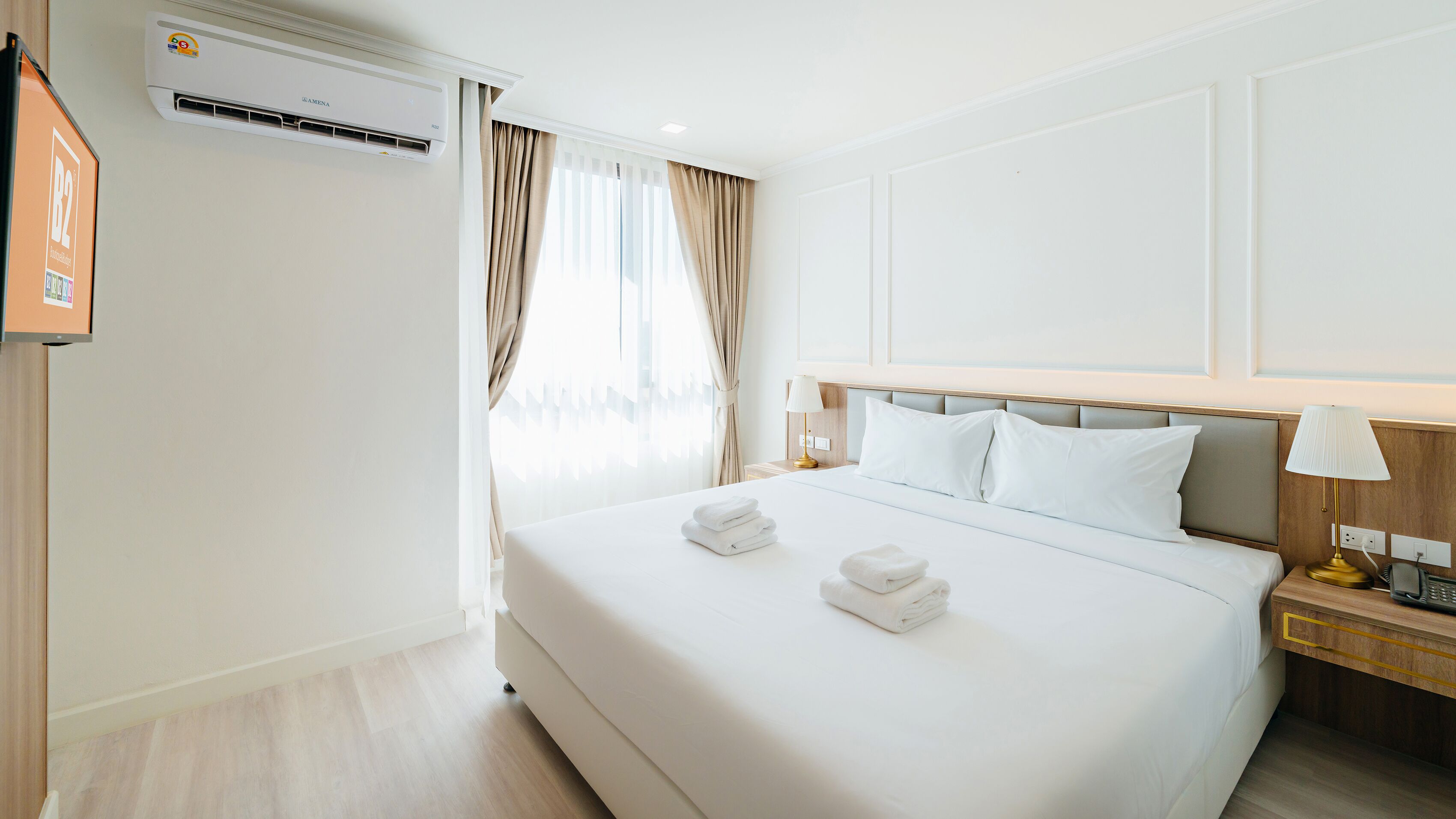Habitación de hotel con una cama grande, una mesita de noche con lámpara, un aire acondicionado y un televisor montado en la pared.