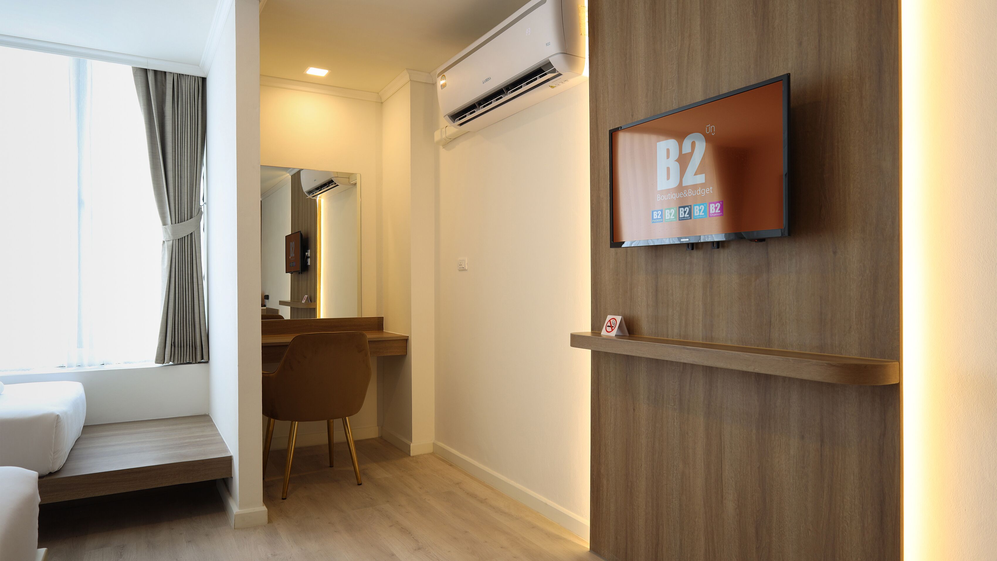 Una habitación de hotel con cama, escritorio, silla, aire acondicionado, televisor montado en la pared y ventana con cortinas.