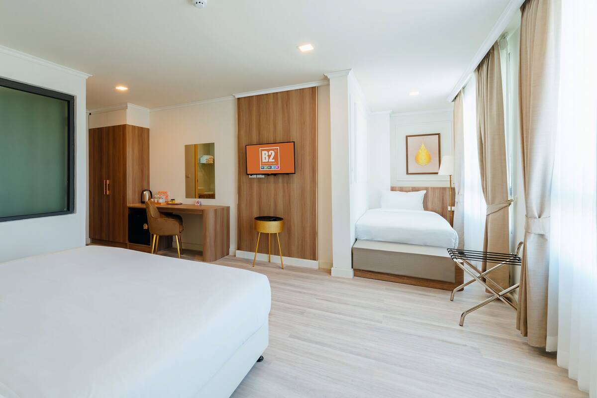 Quarto de hotel com uma cama grande, uma escrivaninha com cadeira, uma mesinha e uma TV fixada na parede.