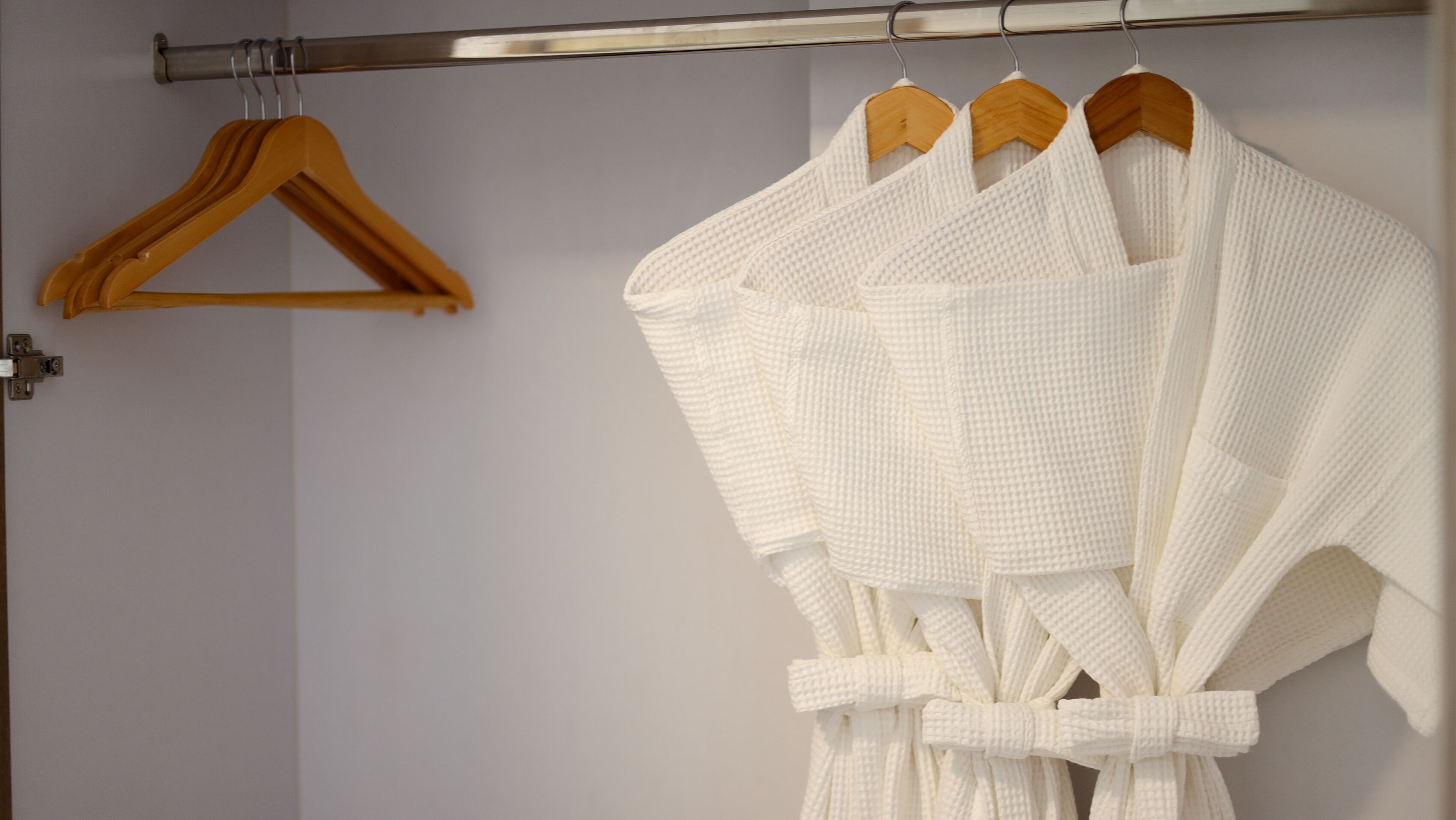 A bathroom with a white towel rack holding three white towels and a wooden hanger.